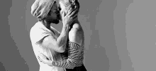 a man and a woman are kissing in a black and white photo . the woman is wearing a striped shirt .
