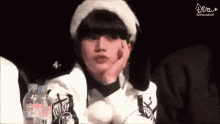 a young man wearing a fur hat and a white jacket is sitting in front of a table with bottles of water .