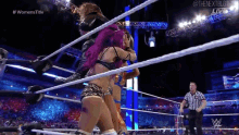 two women are wrestling in a wrestling ring with a referee watching .