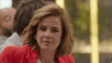 a woman in a red jacket is sitting at a table with a man in the background .