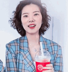 a woman in a plaid jacket is holding a cup with a straw in it