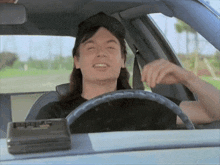 a man with long hair is driving a car with his eyes closed and a cassette player on the dashboard