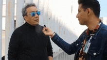 a man wearing sunglasses talks to another man