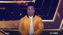 a man in a yellow jacket stands in front of a nbc sign