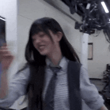 a woman in a striped shirt and tie is standing in a room with a camera .