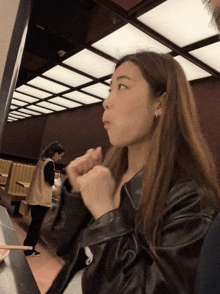 a woman in a leather jacket is sitting at a table eating with chopsticks