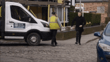 a man in a black coat walks past a white van that says scaffolding
