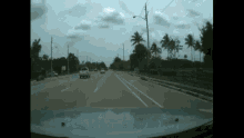a car is driving down a street with palm trees on the side