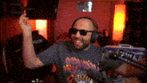 a man wearing headphones and sunglasses is sitting in front of a microphone and giving the middle finger .