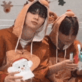 two young men wearing reindeer costumes are sitting next to each other holding a christmas card .