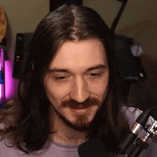 a man with long hair and a beard is sitting in front of a microphone and smiling .