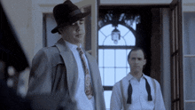 a man in a suit and tie stands next to another man in a bow tie