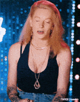 a woman wearing a black tank top and a gold necklace with a pendant