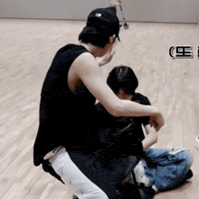 a man in a black tank top sits on a wooden floor