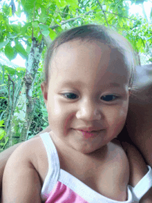 a baby in a pink and white tank top is smiling for the camera