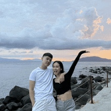 a man and a woman are posing for a picture in front of a body of water