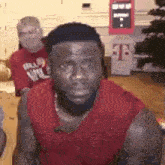 a man with a beard wearing a red tank top is sitting in front of a t-mobile machine .
