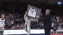 a man holding a framed uconn jersey in front of a crowd