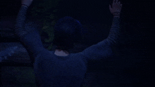 a girl with purple hair and striped sleeves is sitting in the dark with her hands outstretched