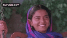 a woman is sitting on a swing wearing a blue scarf and smiling .