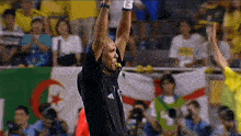 a referee wearing a black adidas shirt holds up his arms in the air