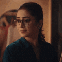 a woman wearing glasses and a blue shirt looks at something