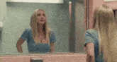 a woman in a blue shirt is looking at herself in a bathroom mirror .