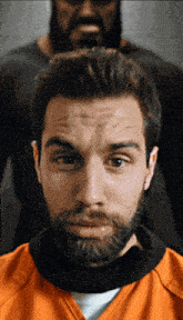 a man with a beard wearing an orange shirt looks at the camera