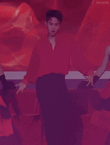 a man in a red shirt and black pants is dancing in front of a red background
