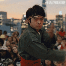 a man in a karate uniform stands in front of a crowd with the hashtag #karatekidmovie