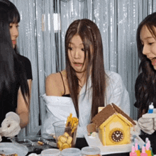 a group of girls are sitting around a table with a gingerbread house and a clock on it