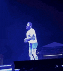 a man in a white shirt and blue shorts is dancing on a stage in front of a crowd .