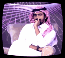 a man in a keffiyeh sits in a chair with his hand to his mouth