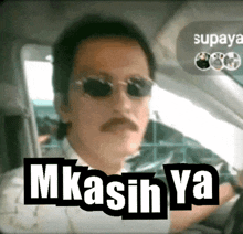 a man wearing sunglasses and a mustache is driving a car with the words mkasih ya written on the screen