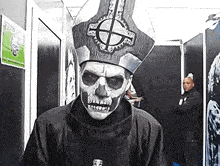 a man wearing a skull mask and a priest hat is standing in a room .