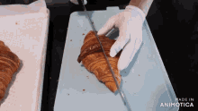 a person is cutting a croissant with a knife on a blue cutting board made by animatica