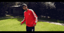 a man in a red adidas jacket stands in a grassy area