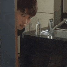 a man is standing in front of a sink and looking at it .