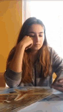 a girl is sitting at a table with her hand on her face