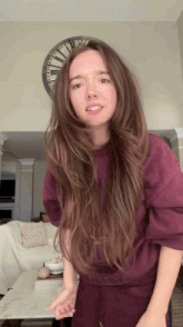 a woman in a purple sweatshirt is standing in front of a clock in a living room
