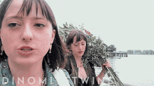 two women are standing in front of a body of water and the words dinomite twins are on the bottom right