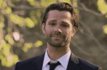 a man with a beard wearing a suit and tie is smiling