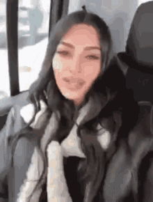 a woman is sitting in the back seat of a car wearing a fur coat and scarf .
