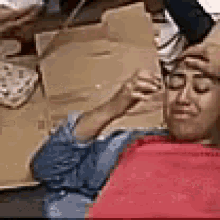 a woman is sitting in a chair with her eyes closed while a man holds a box of pizza .