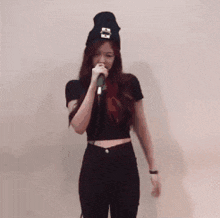 a woman singing into a microphone while wearing a black beanie with the letter c on it