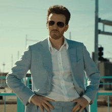 a man wearing a light blue suit and sunglasses stands with his hands on his hips