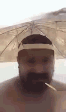 a man with a beard is smoking a cigarette under an umbrella on the beach .