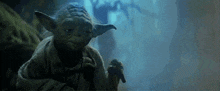 a close up of yoda from star wars holding a cane in a dark cave .