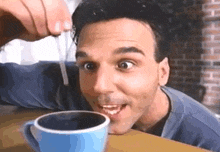 a man is sitting at a table with a cup of coffee and a straw in his mouth .