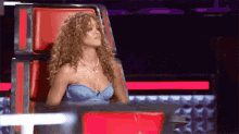 a woman with curly hair is sitting in a red chair with her eyes closed